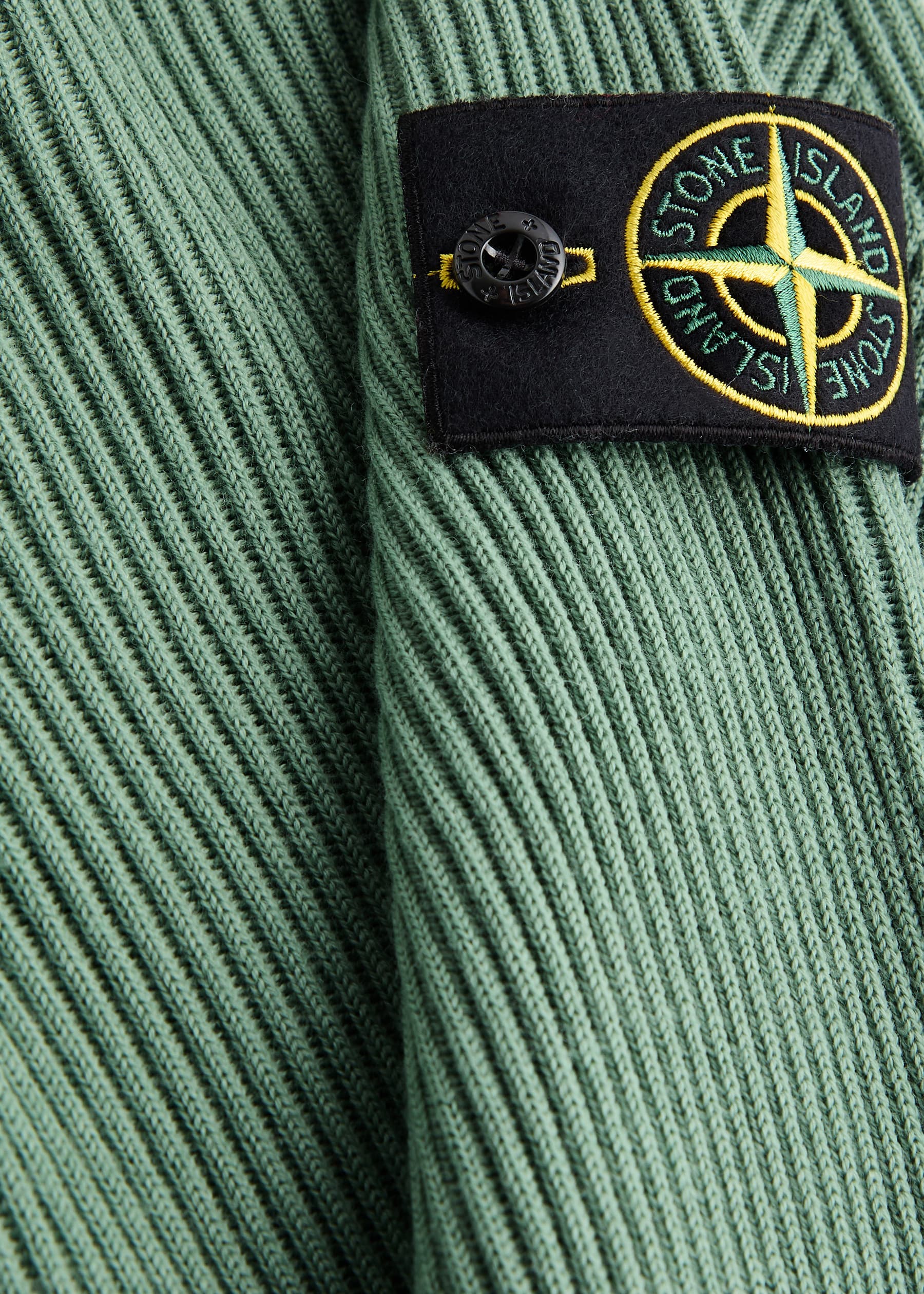 Close-up of a Stone Island badge against green ribbed knit fabric